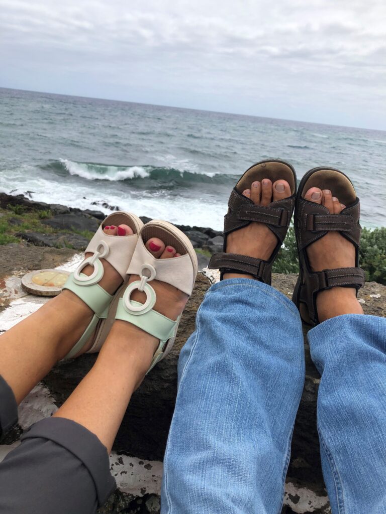 Man and woman sandals relaxing on rock wall overlooking the ocean at Porto Martins last summer.