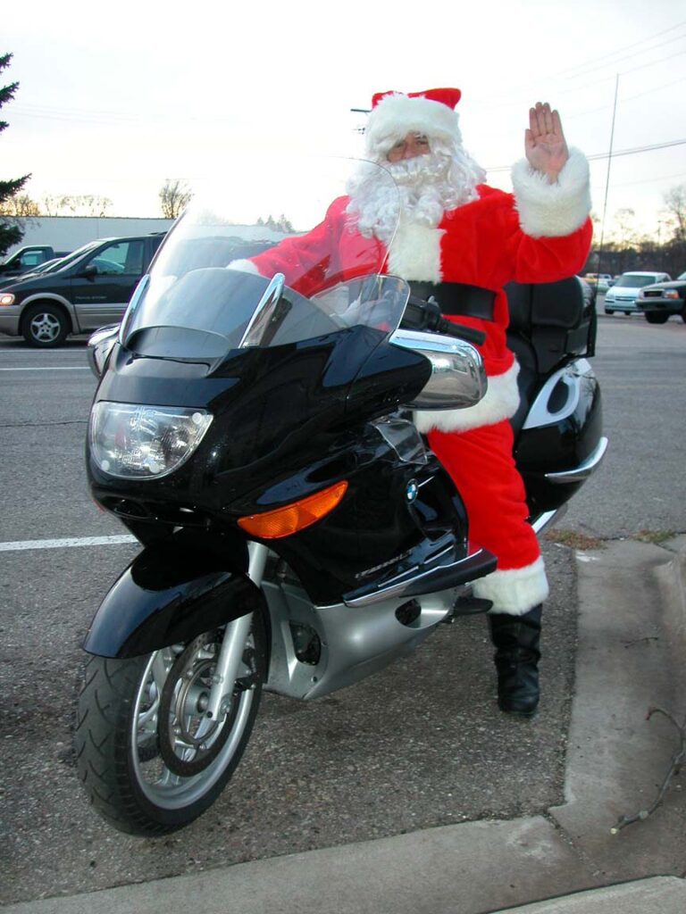 Santa reiding a 2003 BMW K1200LT motorcycle while he waves and smiles.